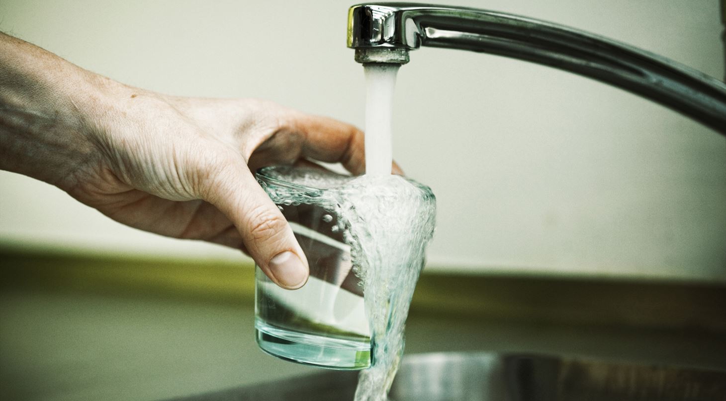 En hnd holder et glas og fylder det med vand fra en vandhane